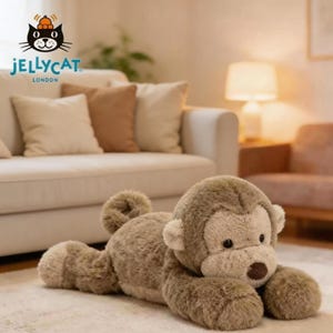 Könnte beinhalten: Ein liegendes Affenspielzeug aus Plüsch in Braun- und Beigetönen. Das Spielzeug hat eine weiche, pelzige Textur mit einem detaillierten Gesicht, einschließlich einer braunen Nase und kleinen, runden Ohren. Das Jellycat London Logo ist sichtbar.