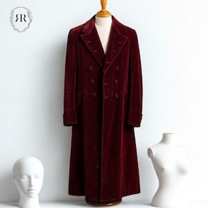 May include: A long, burgundy velvet coat with a double-breasted design. The coat has a notched collar, multiple buttons, and long sleeves. It is displayed on a wooden mannequin against a white background. The coat's length extends to the ankles.
