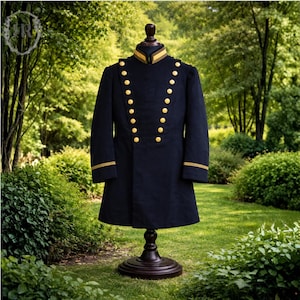 Puede incluir: Un abrigo azul marino de estilo militar con botones y adornos dorados, exhibido en un maniquí de madera oscura. El abrigo tiene cuello alto y mangas largas. El fondo es un jardín verde.