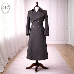 May include: A charcoal gray, double-breasted coat with gold buttons and epaulets, displayed on a wooden dress form. The long coat features a wide collar, two front pockets, and cuffed sleeves. The coat is floor-length.