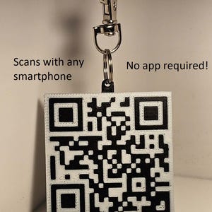 May include: A square, white and black QR code tag with the text "Scans with any smartphone" and "No app required!" attached to a metal clasp and key ring. The QR code is a series of black and white squares.