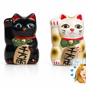 May include: Two beckoning cat figurines, one black and one white with brown patches. Both feature a raised right paw, a red collar with a green glittery bib, a gold bell, and a gold coin held in the left paw with black Japanese characters.