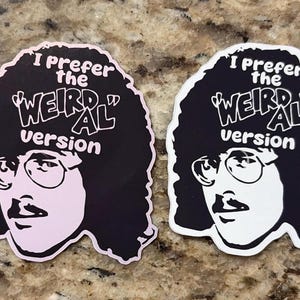 Puede incluir: Dos pegatinas con un retrato estilizado con gafas y bigote, con el texto "I prefer the 'Weird Al' version". Una pegatina es en blanco y negro, la otra es en negro y rosa.