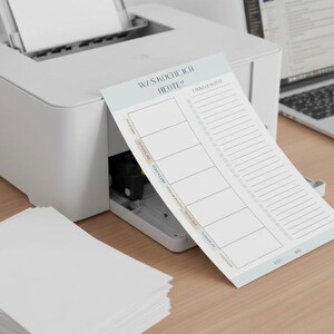 May include: A white printer next to a notepad with the text "WAS KOCHE ICH HEUTE?" and a shopping list. The notepad has sections for each day of the week. A stack of white paper is on the left.