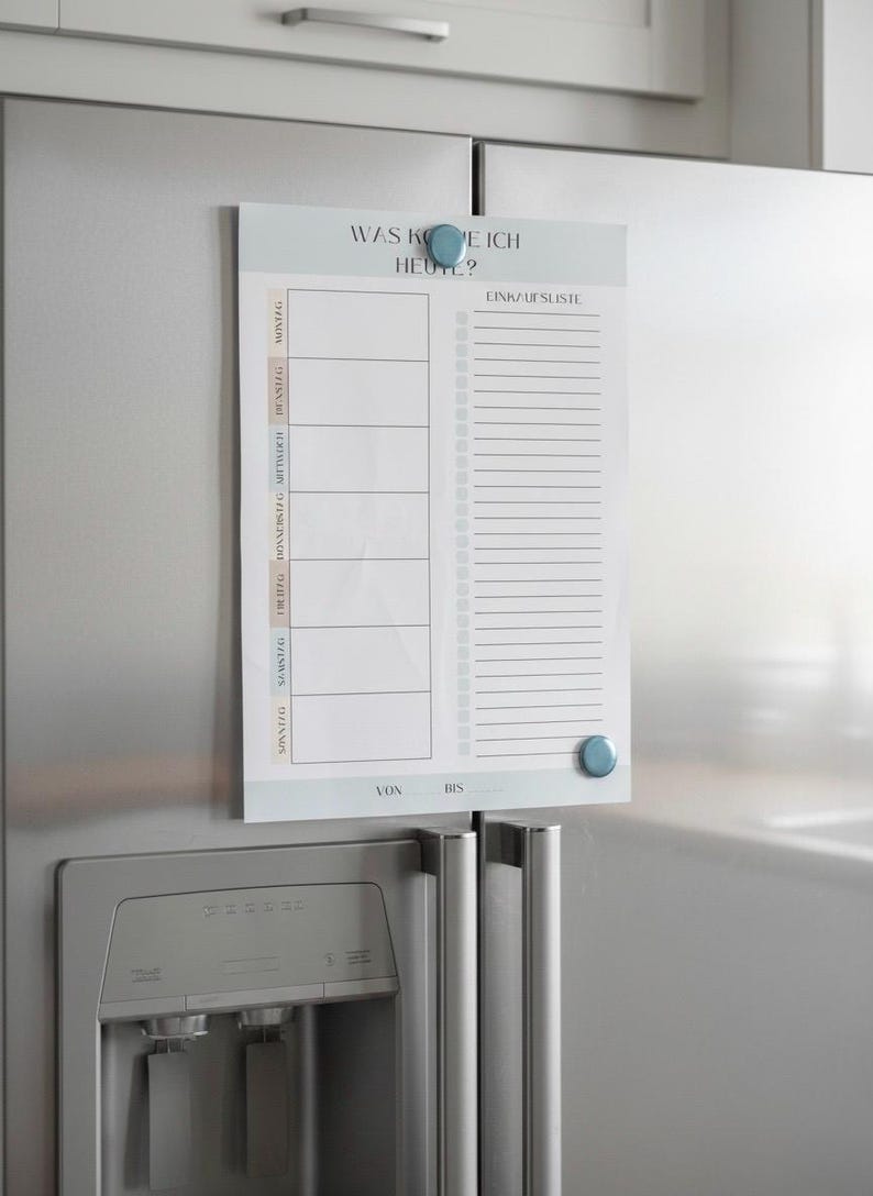 May include: A white magnetic weekly planner with the text "WAS KOE ICH HEUTE?" and "EINKAUFSLISTE" in German. The planner is attached to a stainless steel refrigerator with blue magnetic buttons. It includes sections for each day of the week and a shopping list.
