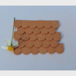 May include: A miniature brown roof made of small, curved tiles. The roof is arranged in overlapping rows, suggesting a building's exterior. A white and yellow flower with a green stem is placed next to the roof.
