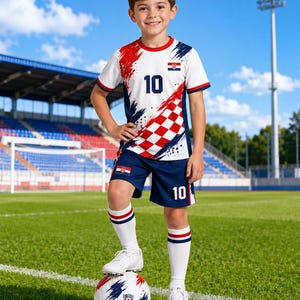 Pu&ograve; includere: Un bambino con una divisa da calcio croata, in piedi su un pallone da calcio su un campo verde. La maglia bianca ha dettagli rossi e blu, il numero 10 e la bandiera croata. Anche i pantaloncini blu navy hanno il numero 10.