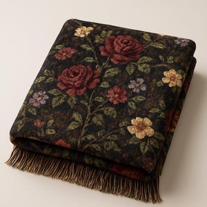 May include: A folded rectangular throw blanket featuring a dark black background with a woven floral pattern of deep red roses, small yellow blossoms, and green leaves. The blanket has a textured appearance and includes a fringe along the edge.