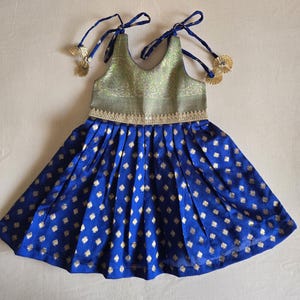 Könnte beinhalten: Blau-goldenes Kleid mit V-Ausschnitt und plissiertem Rock. Das Oberteil ist hellgrün mit einem goldenen Muster. Der Rock ist leuchtend blau mit goldenen herzförmigen Akzenten. Das Kleid hat Bindeträger mit goldenen Quasten.