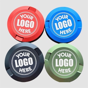 Può includere: Quattro oggetti circolari in rosso, blu, nero e verde. Ognuno ha un cerchio bianco al centro con la scritta "YOUR LOGO HERE". Gli oggetti hanno una finitura metallica e una scanalatura laterale.