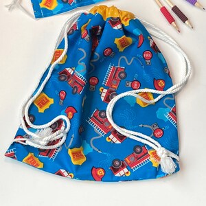 May include: A blue drawstring bag with a white drawstring and a fire truck pattern. The bag has the word "FIRE" printed on it multiple times.