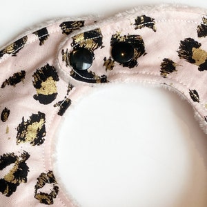 May include: Pink baby bib with a gold and black leopard print and two black snap closures.