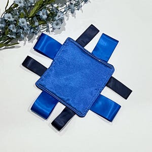 May include: A blue fabric square with four blue and black ribbon ties. The square is made of soft, plush fabric and is perfect for a baby's sensory development.
