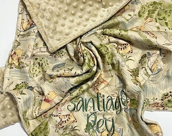 May include: A beige minky dot blanket featuring a printed pattern of Winnie the Pooh characters in a forest setting. The blanket is personalized with the embroidered name Santiago Rey in dark green script lettering across the center fabric.