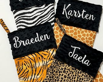 May include: Four black and white Christmas stockings with different animal print designs. The stockings are personalized with the names "Kamryn", "Karsten", "Braeden", and "Jaela".