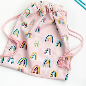 May include: Pink drawstring bag with a rainbow pattern. The bag has a white drawstring and a pink tassel.