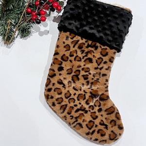 May include: A brown and black leopard print Christmas stocking with a black minky cuff.