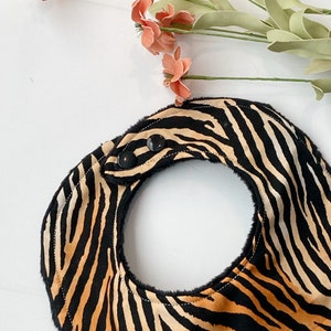 May include: A black and orange tiger print baby bib with black snap closures.
