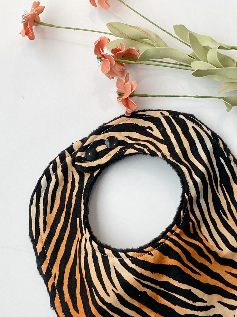 May include: A black and orange tiger print baby bib with black snap closures.