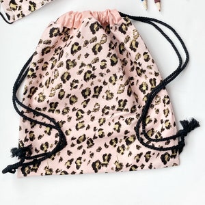 May include: A pink drawstring bag with a leopard print pattern. The bag has black drawstrings and a gold metallic print.