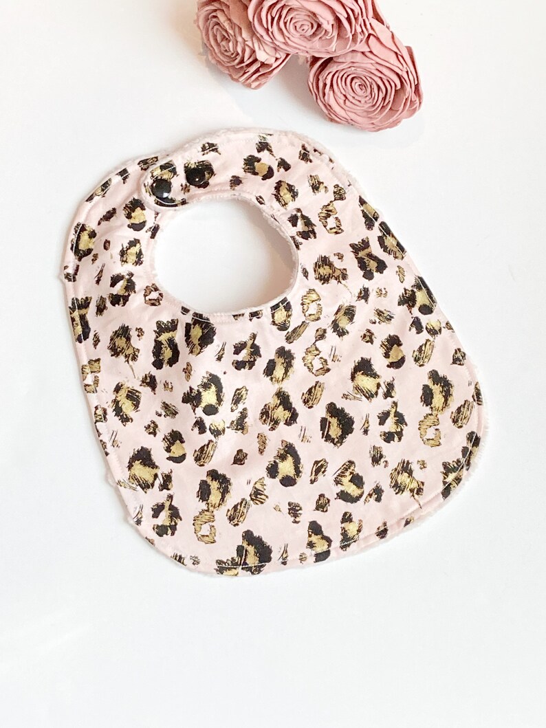 May include: A pink baby bib with a gold and black leopard print pattern.