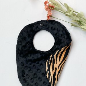 May include: Black and brown zebra print baby bib with a black, textured, padded back.