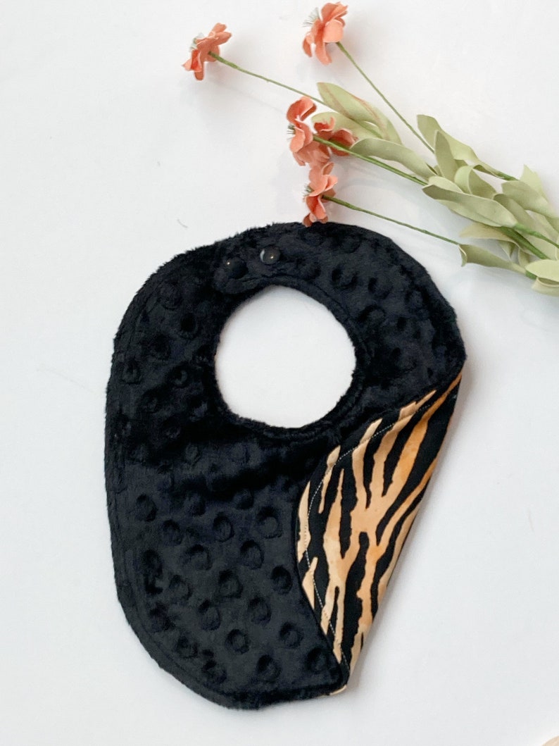 May include: Black and brown zebra print baby bib with a black, textured, padded back.