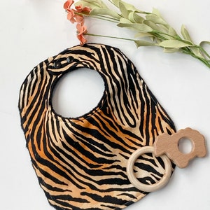 May include: A black and orange zebra print baby bib with two black snaps and a wooden teether ring with a flower-shaped wooden teether attached.