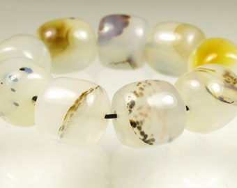 May include: A strand of white agate beads with brown and black inclusions. The beads are round and have a smooth, polished finish.