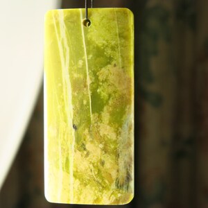 May include: A rectangular green and yellow stone pendant with a hole at the top for hanging. The stone has a marbled pattern with white streaks.
