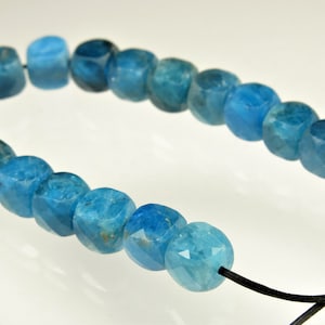 May include: A strand of blue gemstone beads with a faceted, cube-like shape. The beads are strung on a black cord with a knot at the end.