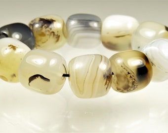 May include: A strand of polished agate beads in shades of cream, tan, gray, and black. The beads are rounded and strung together on a black cord, showcasing natural patterns and variations in color. The beads are approximately 1.5 cm in diameter.