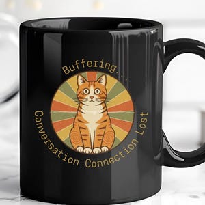 May include: Black ceramic mug featuring a cartoon orange tabby cat inside a circular design with the words "Buffering... Conversation Connection Lost". The mug has a glossy finish and a large handle.