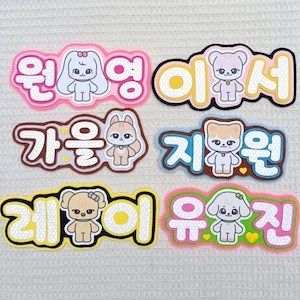 Op de afbeelding: Zes decoratieve gestanste stickers met cartoon-dierfiguren en Koreaanse tekst. Elke sticker heeft een unieke gekleurde rand, waaronder roze, zwart, bruin, blauw, geel en groen, met witte honingraatpatronen op de letters.