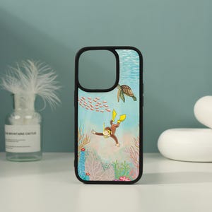 May include: A black phone case featuring an underwater scene with a brown monkey wearing yellow swim fins and a snorkel mask, a green sea turtle, a school of small red fish, and various colourful coral formations against a light blue water background.