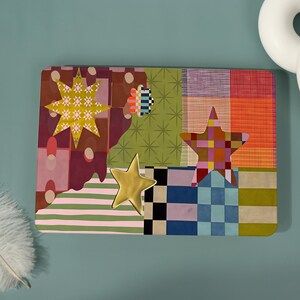 May include: A rectangular laptop skin featuring a vibrant collage of patterns including green starbursts, pink and white stripes, checkered squares, and solid blocks of orange and purple, accented by three distinct star-shaped graphic overlays.