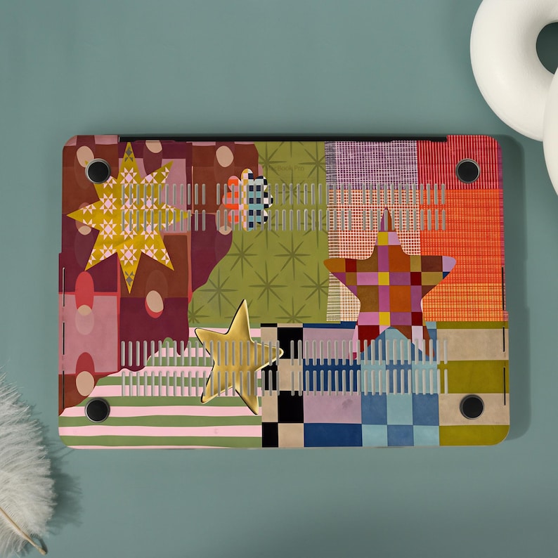 May include: A laptop hard shell case featuring a multi-colored patchwork design with various geometric patterns, including stripes, checks, and star shapes in shades of yellow, orange, red, green, blue, and pink, with four black circular feet.