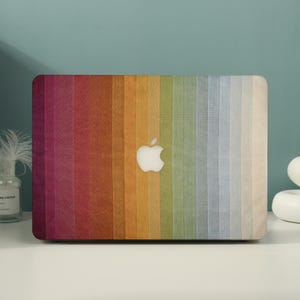 May include: A laptop hard shell case featuring a vertical gradient pattern of colors ranging from deep magenta and red on the left to orange, yellow, green, blue, and light cream on the right, with a central cutout for the Apple logo.