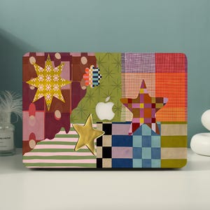 May include: A laptop hard shell case featuring a multi-colored patchwork design with various patterns including stripes, checkers, and star shapes. The surface displays a yellow star, a multi-colored star, and a white Apple logo in the center.