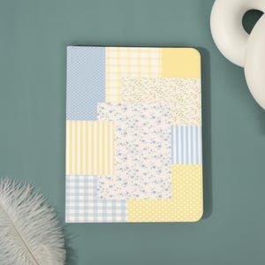 May include: A rectangular tablet case featuring a patchwork design of various patterns in soft yellow and light blue. The surface displays a mix of polka dots, gingham checks, vertical stripes, and small floral prints arranged in a grid-like layout.