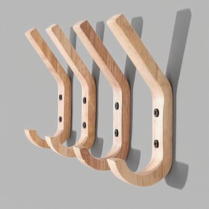 Puede incluir: Cuatro percheros de madera montados en una pared gris. Los percheros son de madera clara con un diseño curvo y tornillos negros. Los percheros están espaciados uniformemente, creando una estética minimalista y funcional.