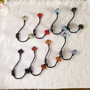 May include: A collection of decorative wall hooks with black metal frames and colorful, glass-like knobs. The knobs are in various colors, including red, orange, blue, and green. The hooks are designed for hanging items and add a touch of elegance.