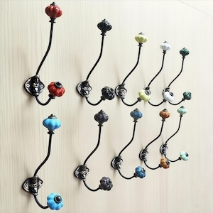 May include: A set of decorative wall hooks with black metal frames and colorful ceramic knobs. The knobs come in various colors, including red, blue, green, and yellow. The hooks are mounted on a light-colored wall.