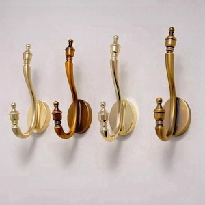 Puede incluir: Cuatro perchas de pared decorativas en acabados metálicos variados: dorado, bronce y latón. Cada gancho presenta un diseño curvo con remates decorativos, montado sobre una placa trasera redonda. Ideal para colgar abrigos, sombreros u otros objetos.