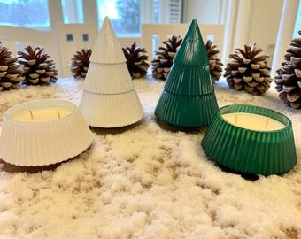 Puede incluir: Velas blancas y verdes con forma de árbol de Navidad y candelabros a juego con mechas encendidas. Las velas y los candelabros están sobre una superficie cubierta de nieve artificial, con piñas de pino en el fondo.