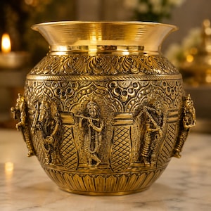 May include: An ornate, gold-coloured brass pot with detailed relief carvings. The pot features figures and floral patterns. The rim flares outwards, and the base is rounded. The pot is likely used for decorative or ceremonial purposes.