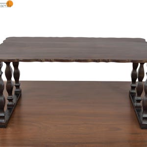 May include: A dark brown wooden coffee table with a scalloped edge. The table has ornate, turned legs and a rectangular top. The table is set on a brown surface and is against a white background.
