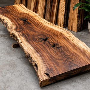 Può includere: Un piano tavolo in legno a bordo vivo caratterizzato da una ricca venatura marrone con nodi naturali e bordi irregolari. La superficie presenta una finitura lucida che mette in risalto la texture organica del legno e le variazioni di colore.