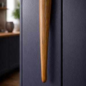 May include: A wooden cabinet handle with a tapered design. The handle is a warm brown color with visible wood grain and is mounted on a dark blue cabinet door. The handle has a smooth, rounded top.