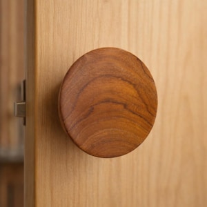 May include: Close-up of a round, wooden cabinet knob. The knob is a warm brown color with visible wood grain. It is mounted on a light-colored wooden cabinet door, suggesting a focus on home decor and furniture.